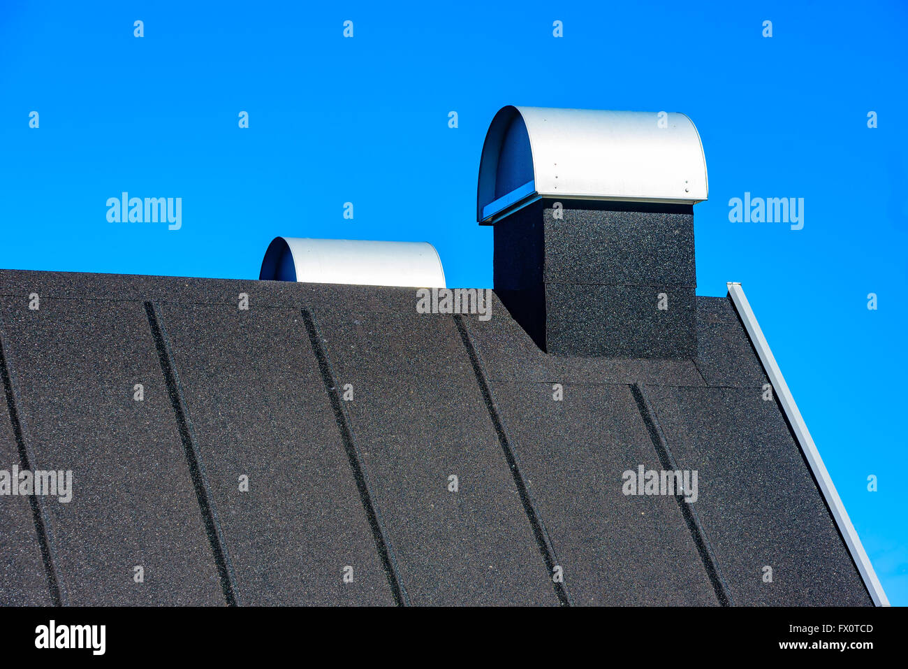 Auf dem Dach mit überdachten Schornsteinen. Dach ist schwarz und mit Teerpappe oder Dachpappe bedeckt. Blauen Himmel im Hintergrund. Stockfoto