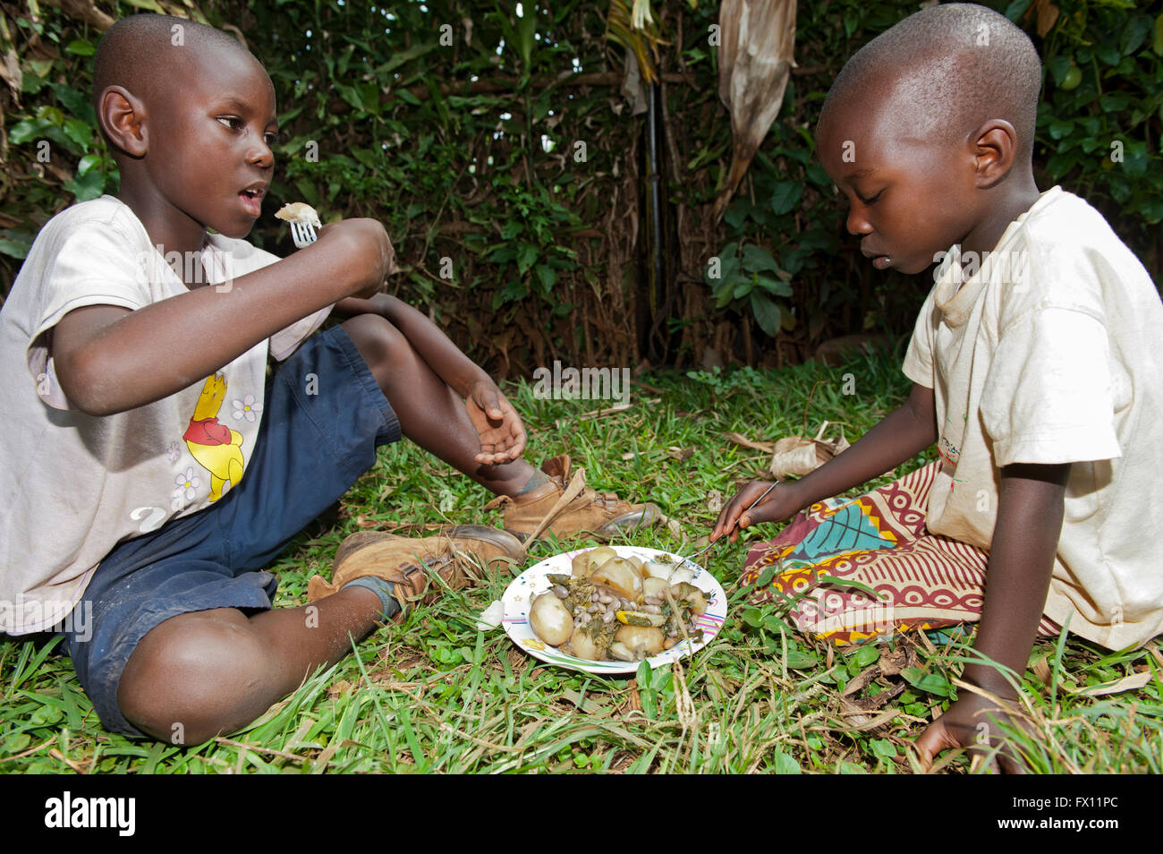 Bruder und Schwester teilen einen Teller gekochte Pootatoes und Bohnen zum Mittagessen, Ruanda. Stockfoto