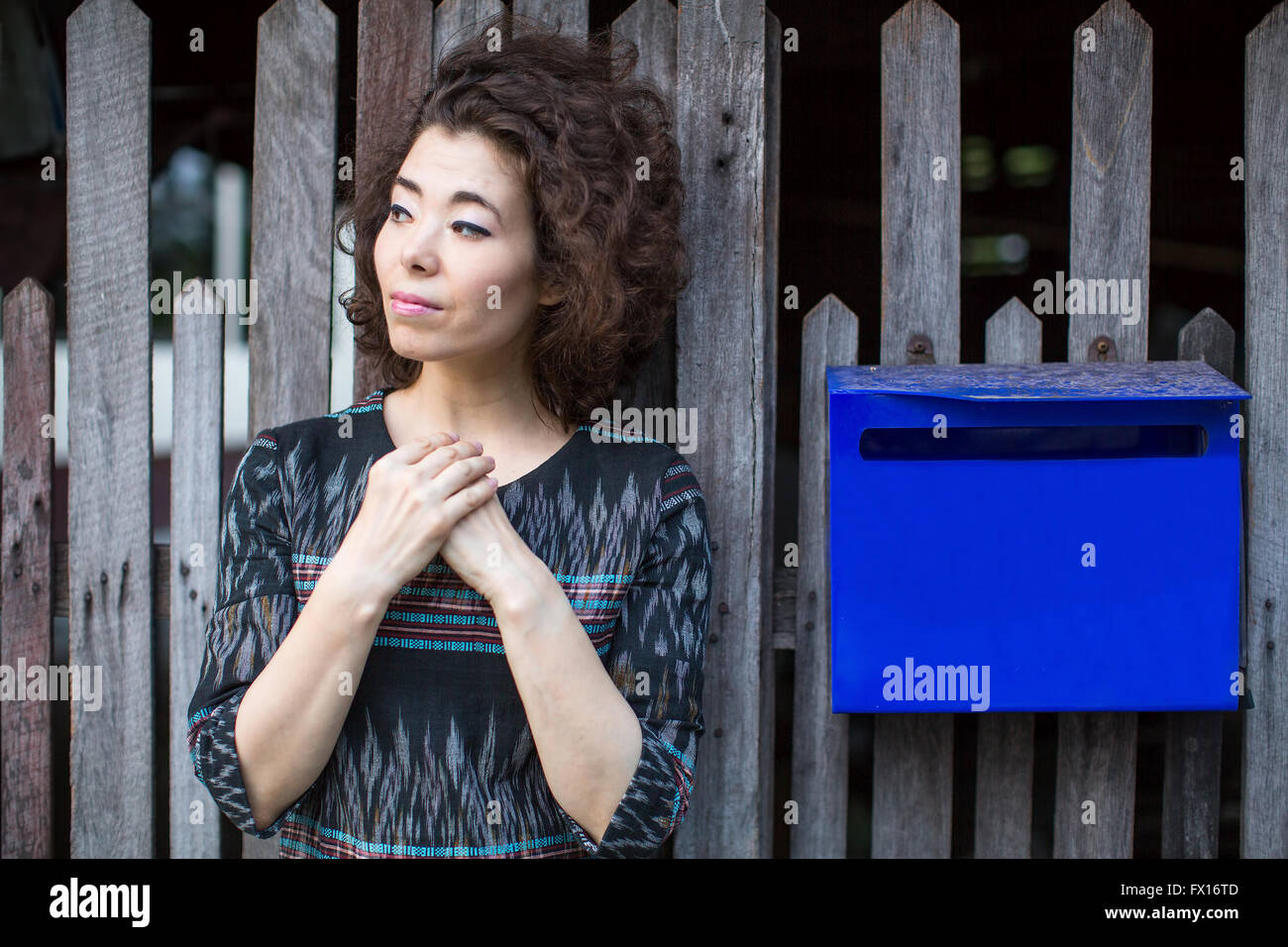 Asiatische Frau steht in der Nähe des Zauns mit einem blauen Postfach. Stockfoto