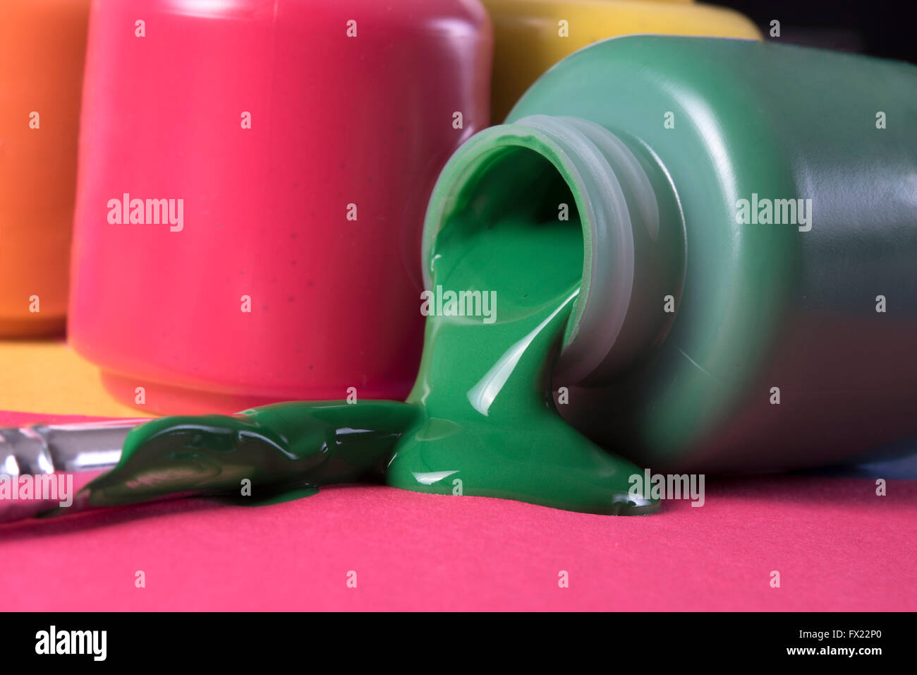 grüne Farbe verschütten aus Behälter, blau, orange und rote Farben im Hintergrund Stockfoto