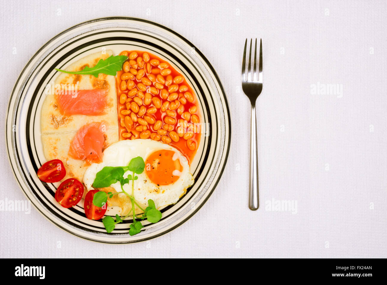 Frühstücksteller mit Spiegelei, gebackene Bohnen, Kartoffelkuchen und Schottischer Räucherlachs von oben Stockfoto