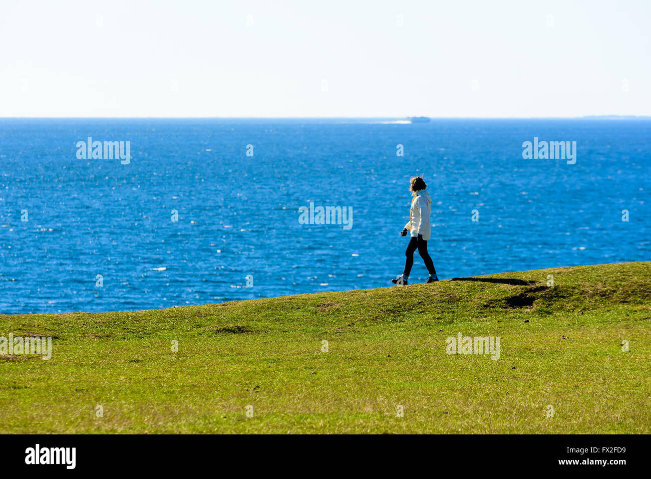 Kaseberga, Schweden - 1 April, 2016: Frau zu Fuß auf den Hügel entlang der Küste auf das Meer schauen und Beobachten ein Boot i Stockfoto