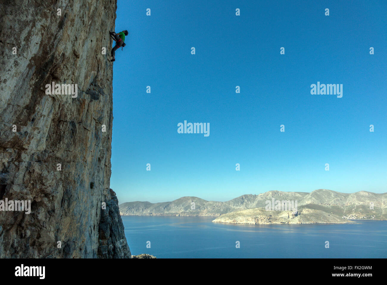 kleinen Kletterer auf steilen Felsen mit blauen Meer hinter Silhouette Stockfoto