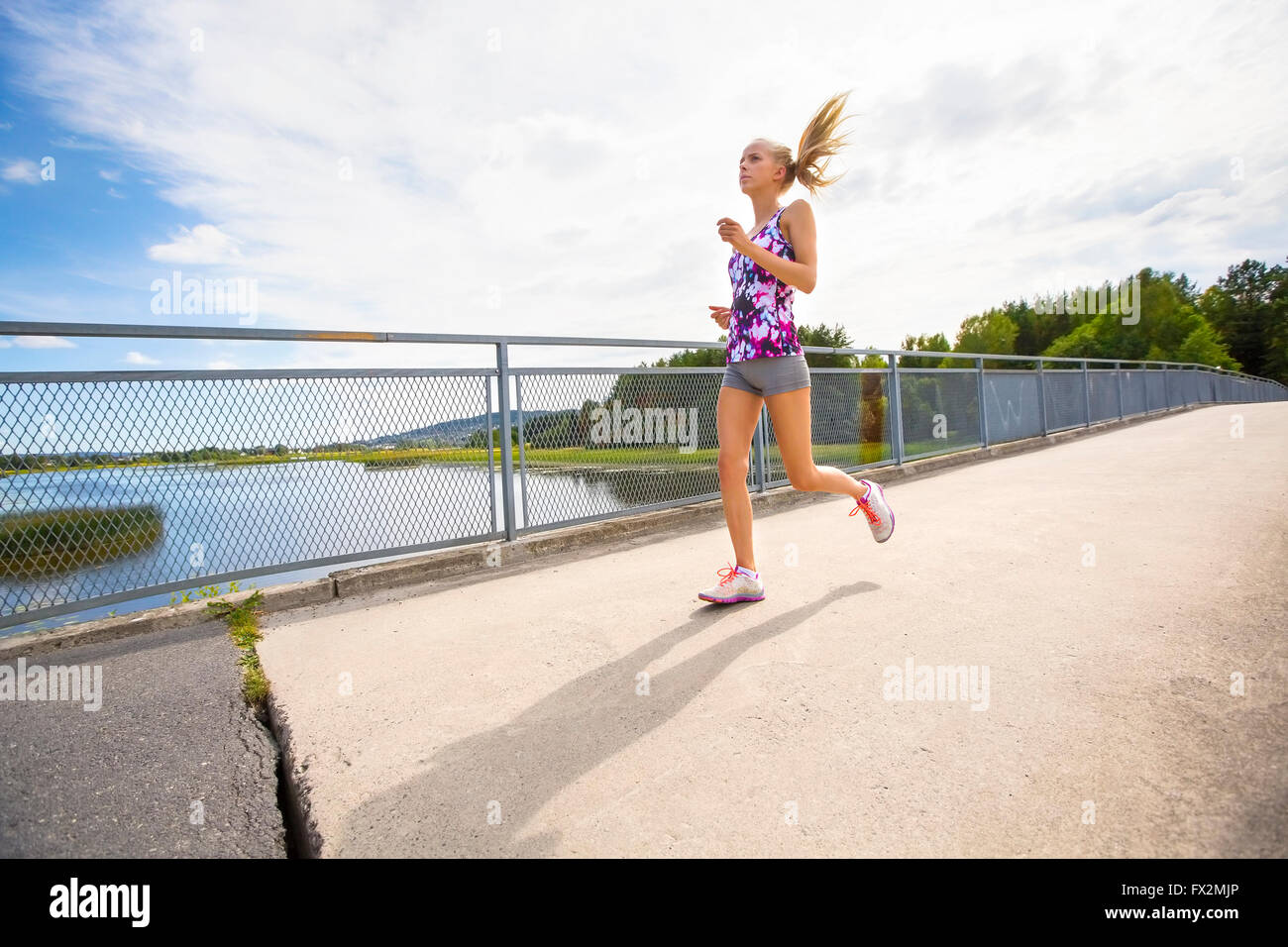 Motivierte junge Frau läuft schnell auf Brücke über einem See Stockfoto