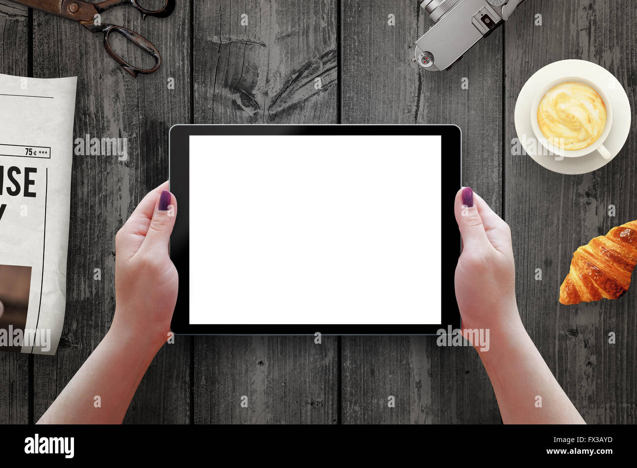 Tablet mit isolierten Bildschirm in Frau die Hände. Morgen mal mit Zeitung, Croissant, Kaffee am Tisch. Stockfoto