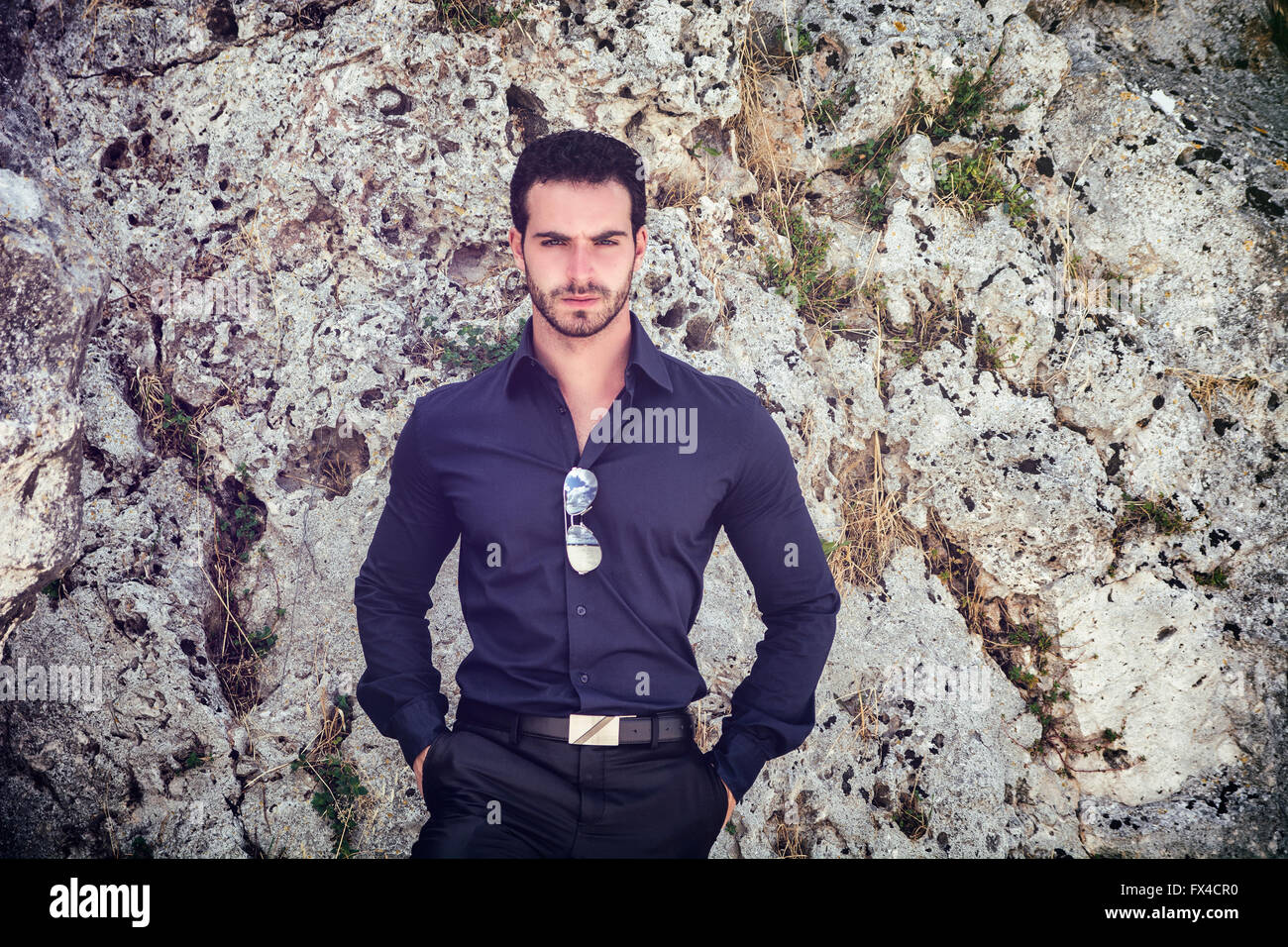 Eine halbe Stelle erschossen eines wunderschönen jungen Geschäftsmann gegen Boulder mit Händen in den Taschen und in die Kamera schaut. Stockfoto