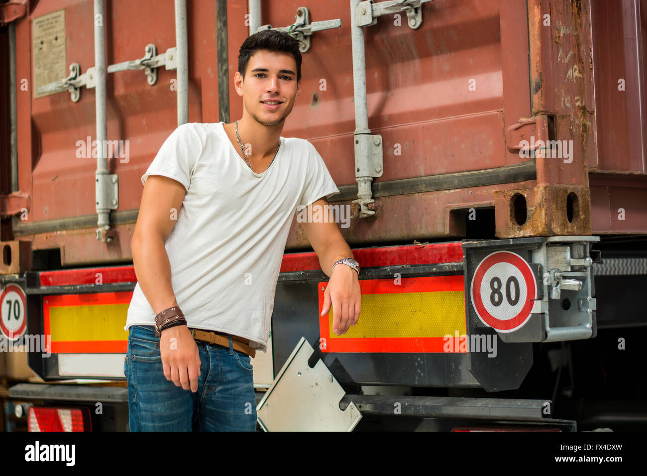 Taille bis Porträt des jungen lächelnd Mann neben LKW - entladen von Fracht aus Container Stockfoto