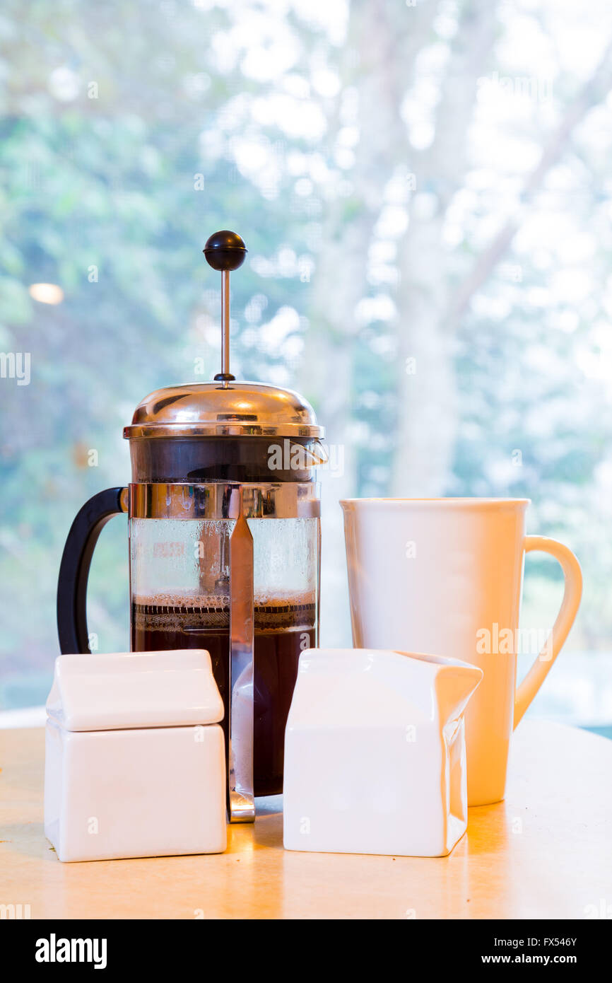 Kaffee wird in den frühen Morgenstunden in einem französischen Presse zusammen mit Sahne und Zucker auf dem Küchentisch gemacht. Stockfoto