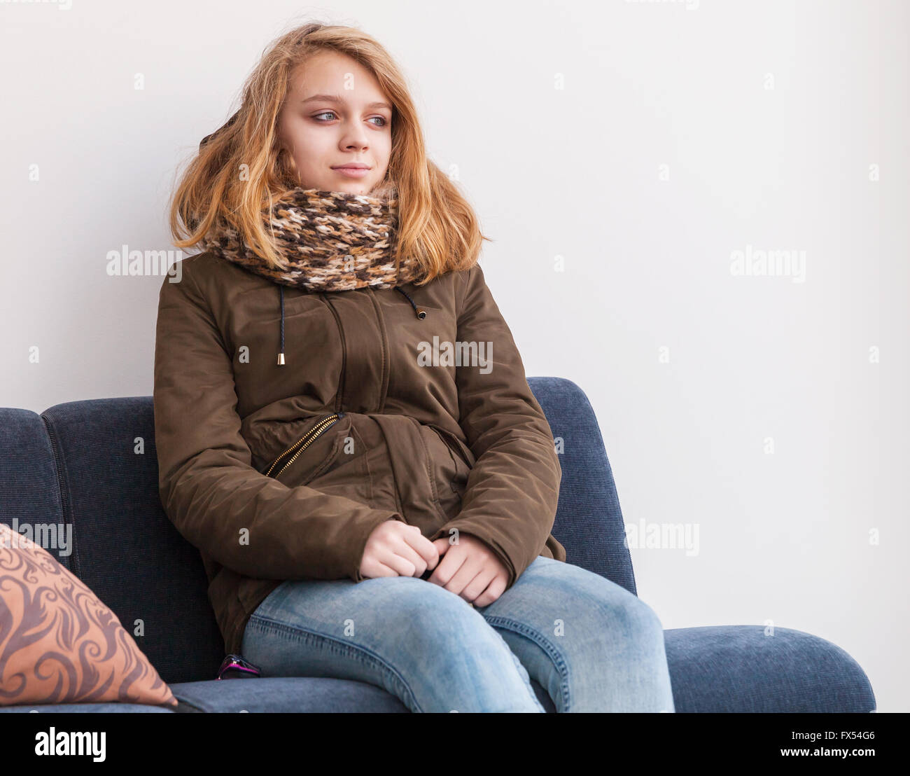 Blonde kaukasische Teenager-Mädchen in warme Kleidung über weiße Wand auf Sofa sitzen Stockfoto