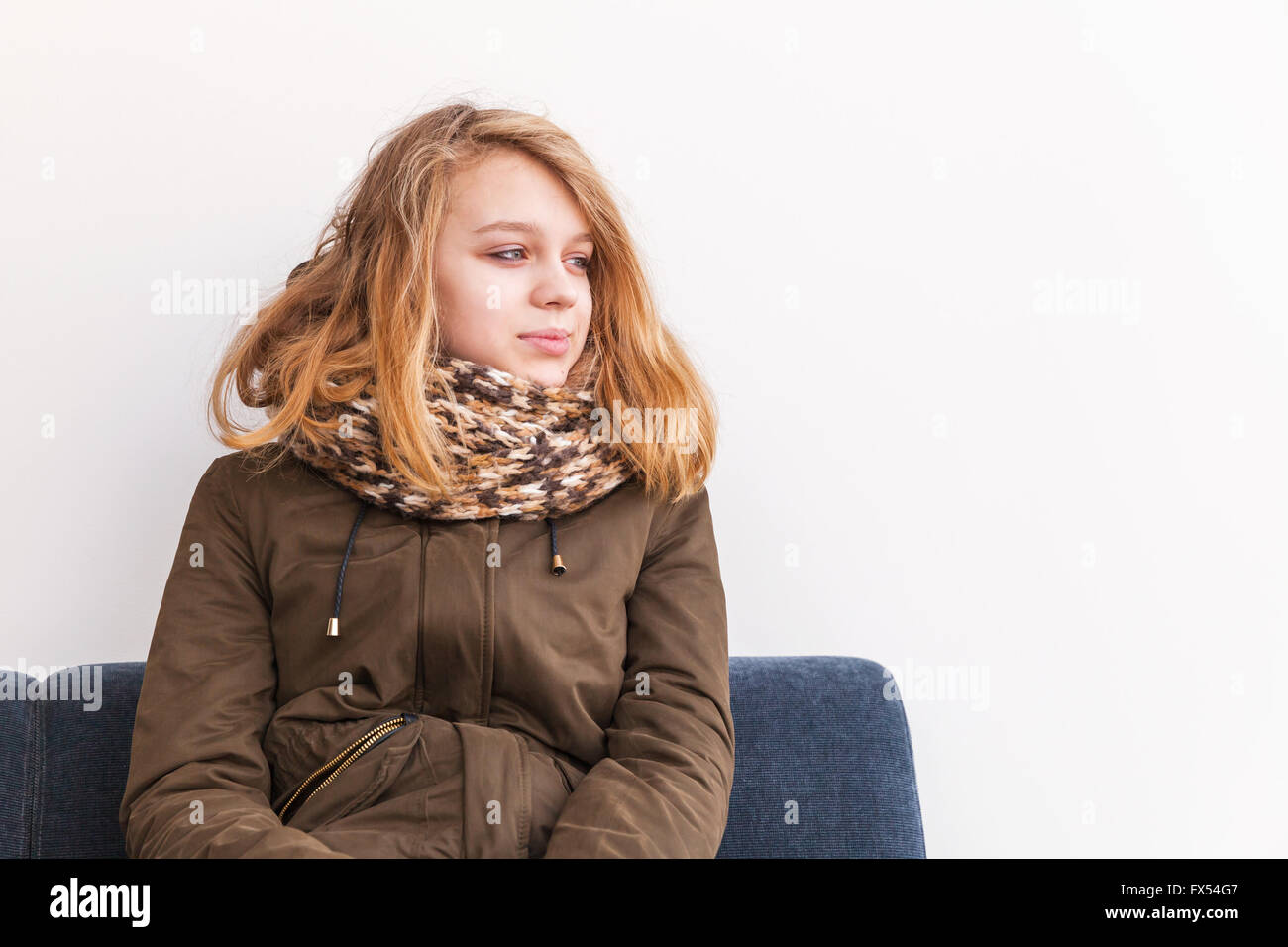 Schöne blonde kaukasische Teenager-Mädchen in warme Kleidung über weiße Wand auf Sofa sitzen Stockfoto