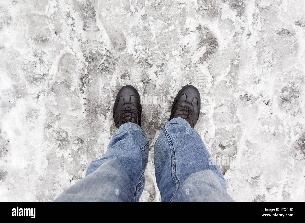 Männliche Füße in Blue Jeans auf nassen schmutzigen Schnee stehen Stockfoto