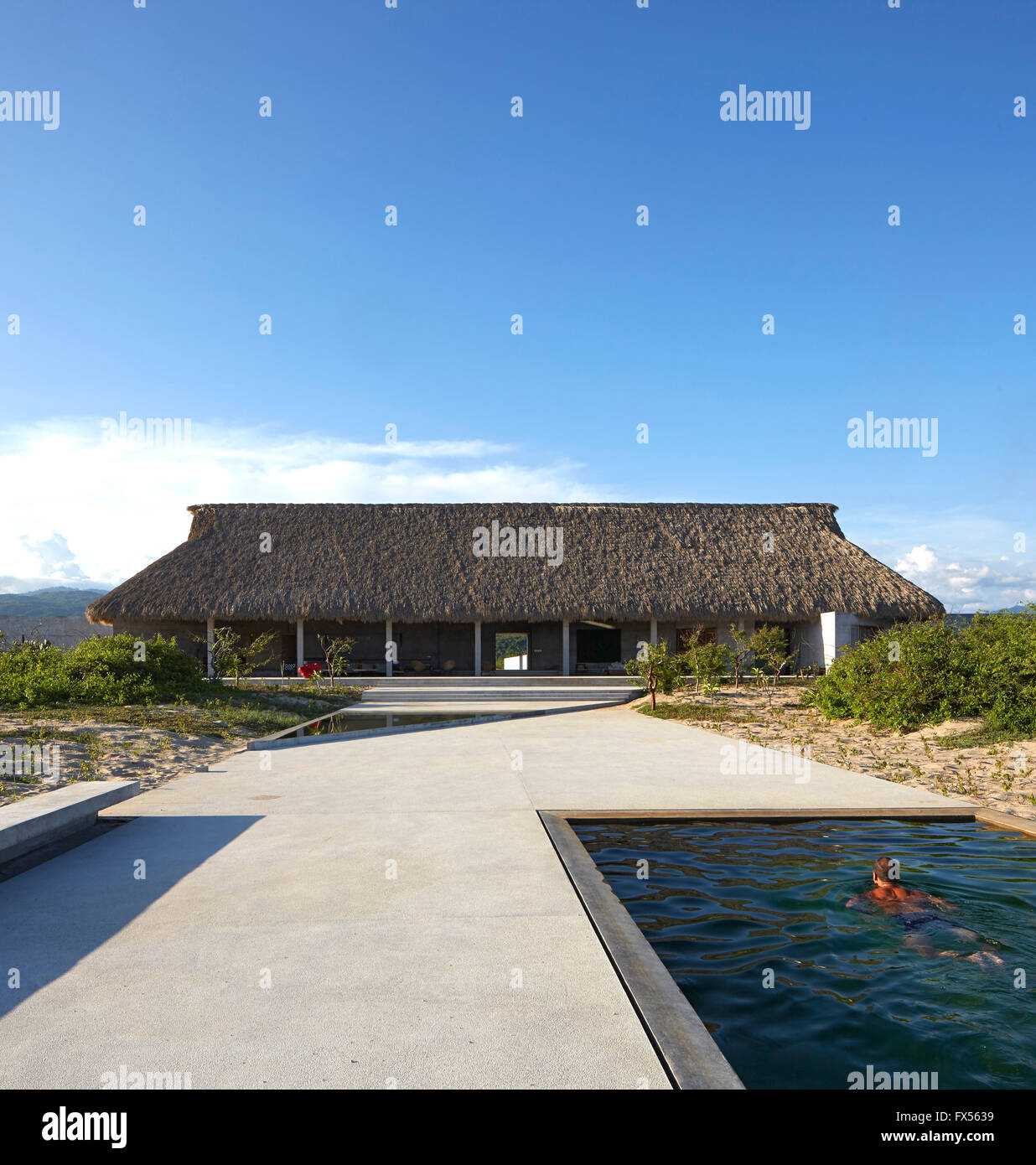 Ozean-Seitenansicht zur wichtigsten Palapa mit Künstler im Pool. Casa Wabi, Puerto Escondido, Mexiko. Architekt: Tadao Ando, 2015. Stockfoto