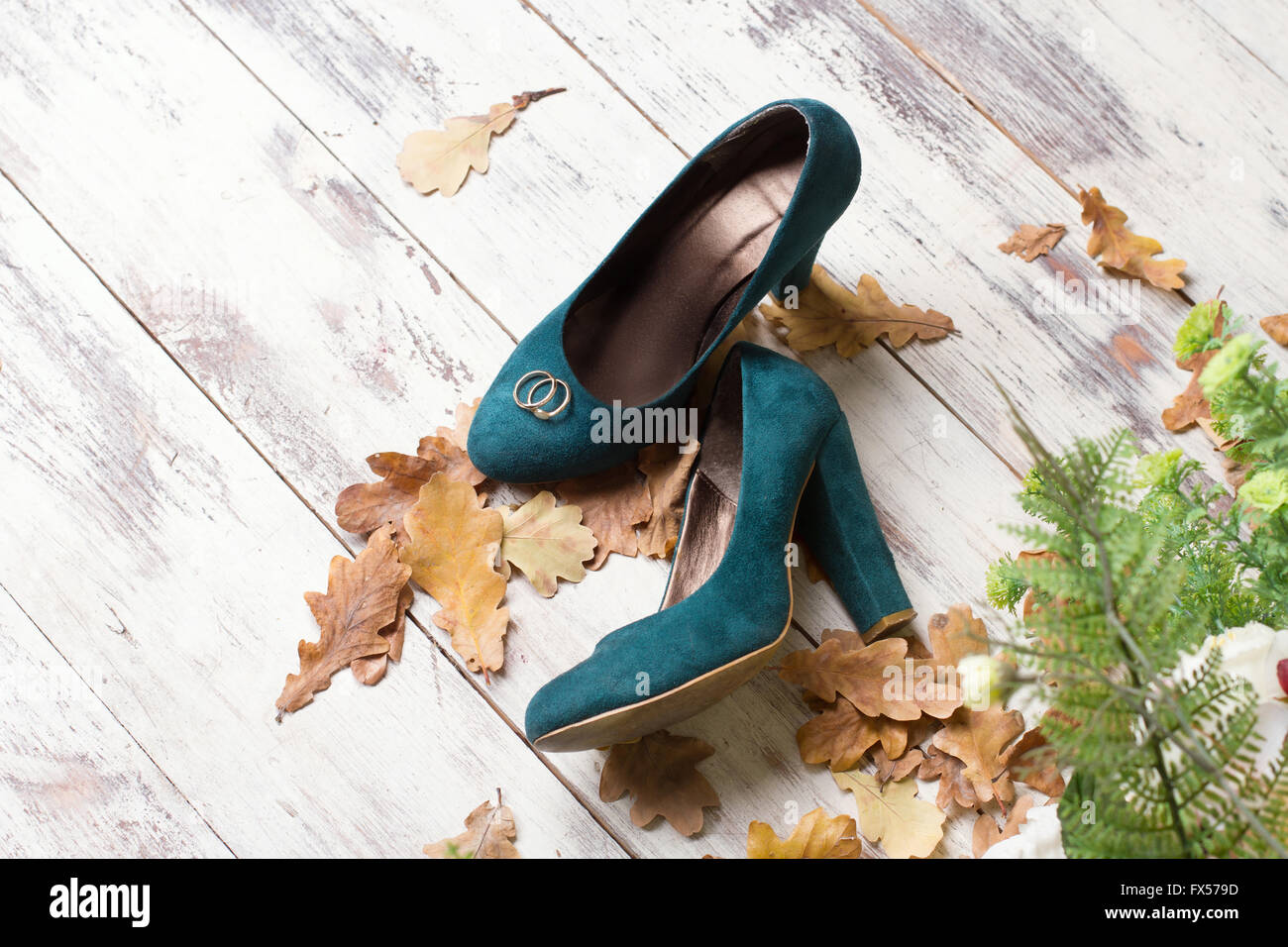 Trauringe auf grünem Veloursleder Schuhe. Hölzerne Hintergrund mit Herbstlaub und grünem Farn. Stockfoto