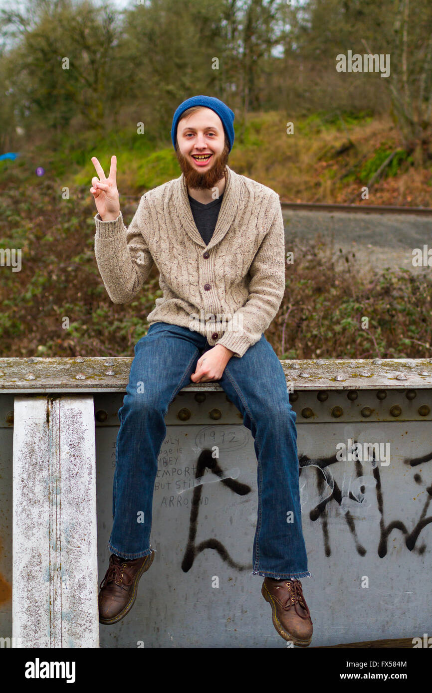 Hippie-Mann sitzt auf einer Brücke ein Friedenszeichen in diesem trendigen Hipster Fashion Porträt zu geben. Stockfoto