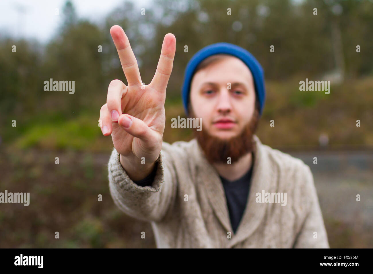 Hippie-Mann sitzt auf einer Brücke ein Friedenszeichen in diesem trendigen Hipster Fashion Porträt zu geben. Stockfoto