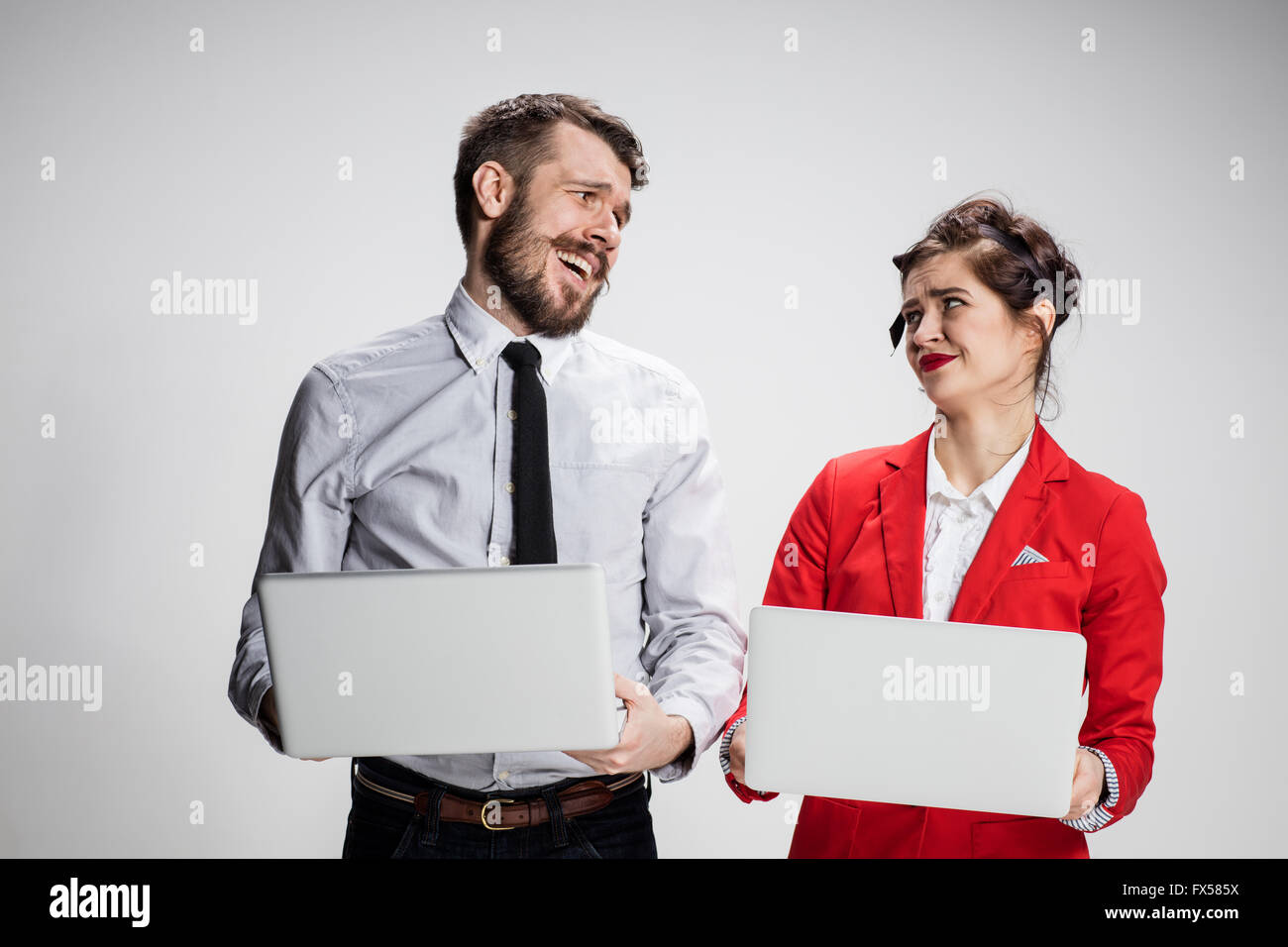 Der junge Geschäftsmann und Geschäftsfrau mit Laptops kommunizieren auf grauem Hintergrund. Das Konzept der Beziehung von Kollegen Stockfoto