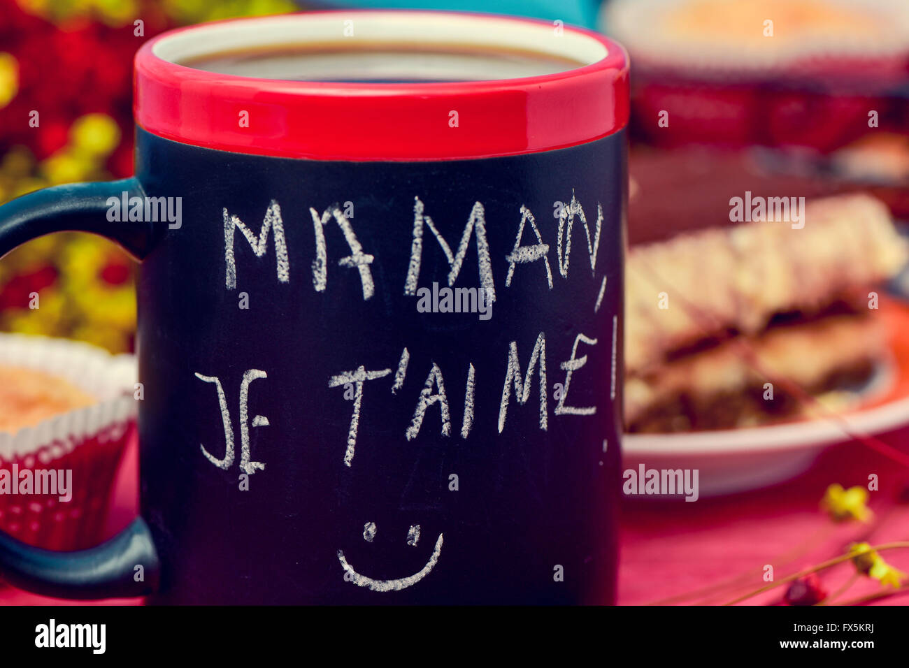 der Satz Maman Je t Aime, ich liebe Sie Mama im französischen handschriftlich mit Kreide in eine schwarze Tasse mit Kaffee, mit einigen Muffins in t Stockfoto