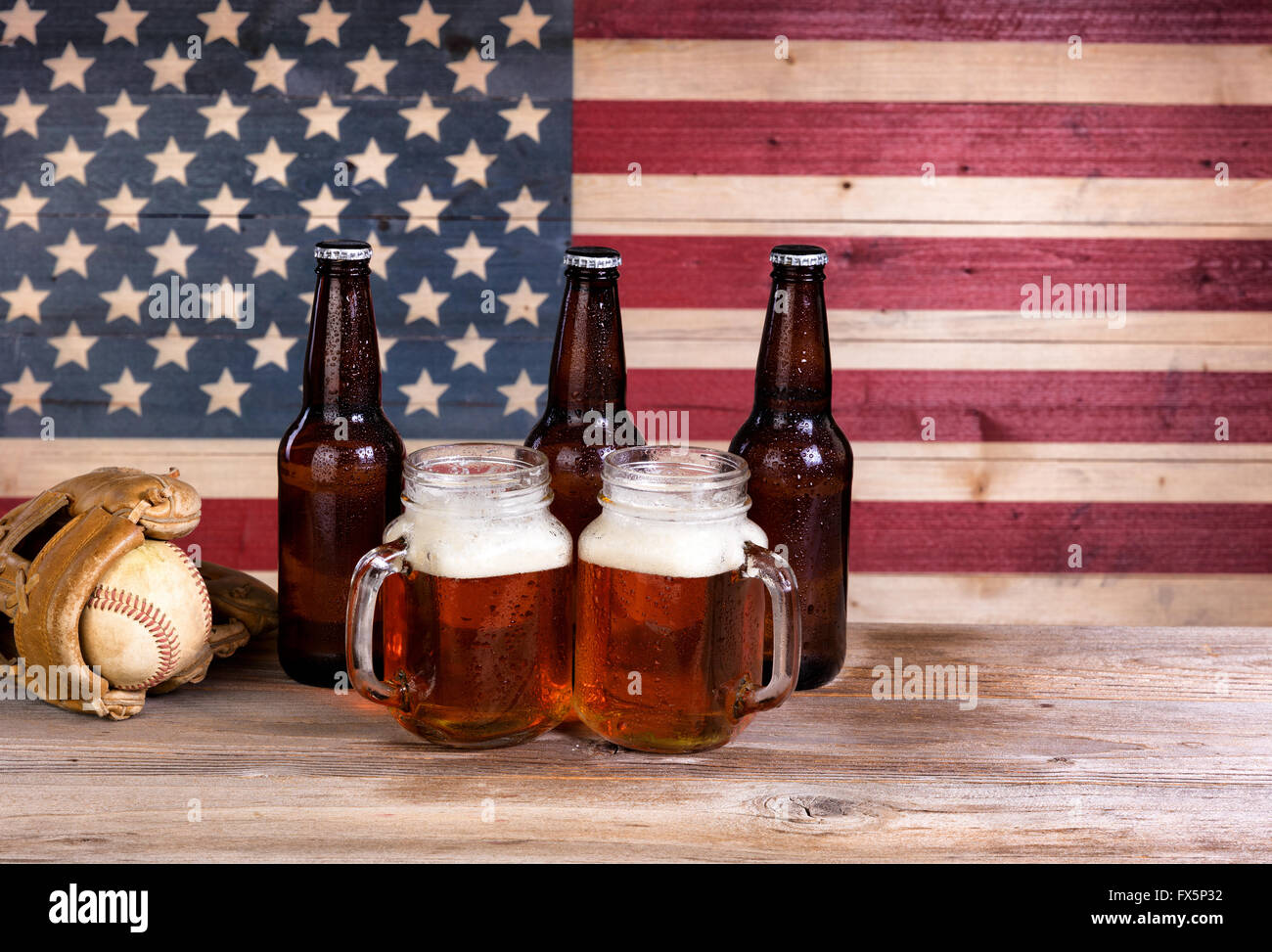 Zwei Bier Gläser gefüllt mit Bier, vollen Flaschen und Baseball Handschuh mit Vintage Holz USA-Flagge im Hintergrund. Stockfoto