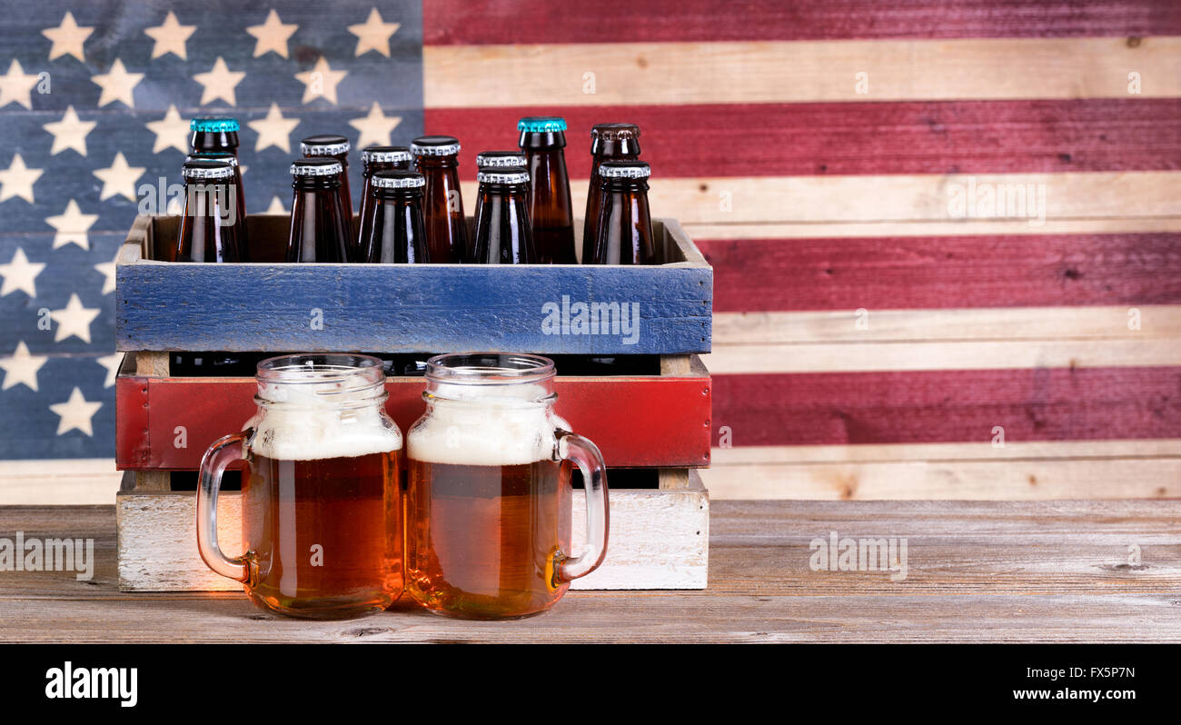 Zwei Bier Gläser gefüllt mit Bier, Kiste mit Ungeöffnete Flasche und Vintage Holz USA-Flagge im Hintergrund. Holiday Party Konzept. Stockfoto