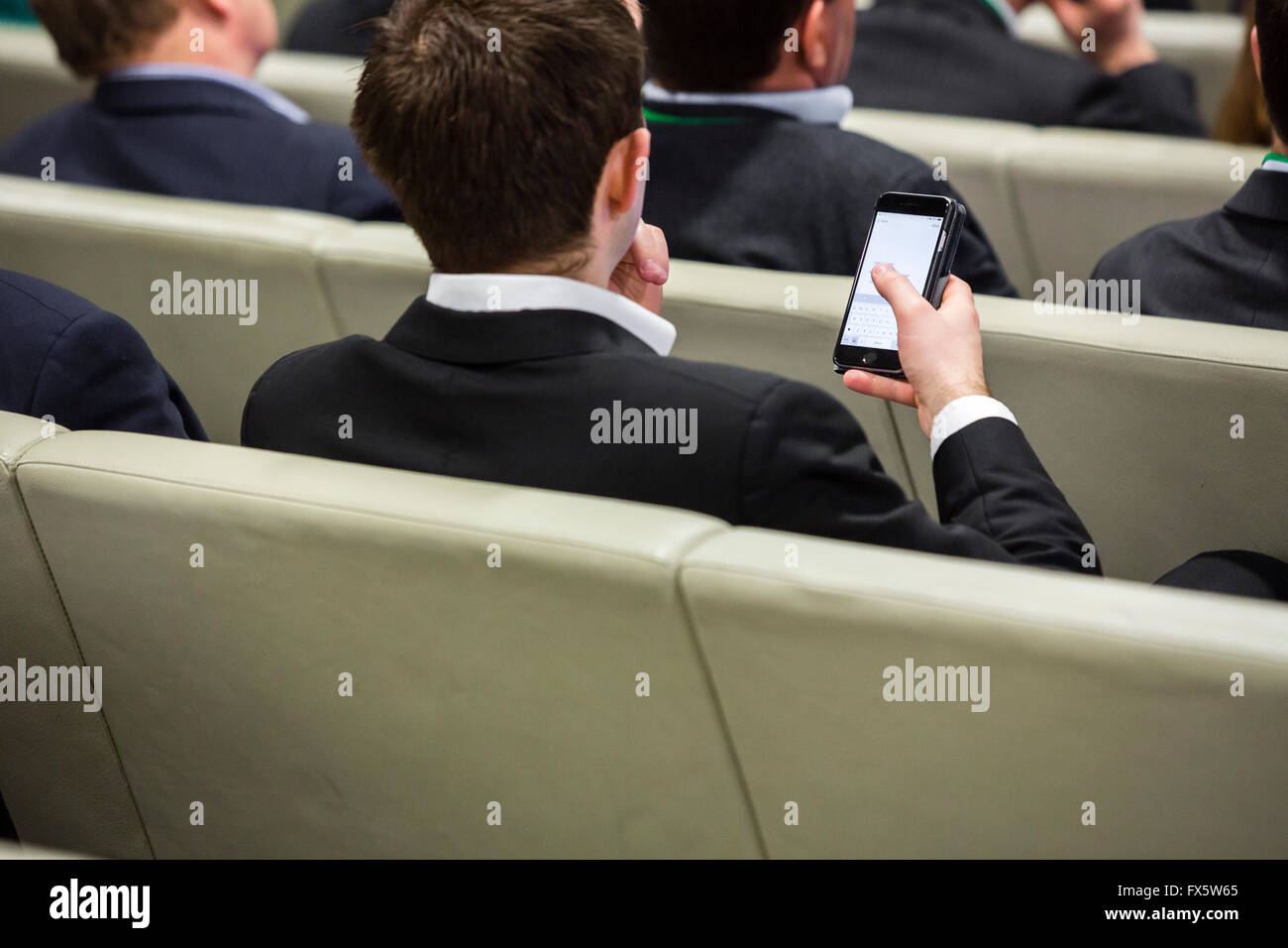 Sitzreihen in einem Auditorium mit sitzendem Publikum und Mann auf einem Mobiltelefon. Stockfoto