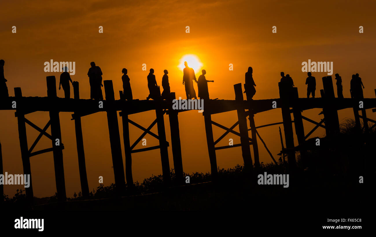 Eine Gruppe von Menschen, die über die hölzerne U-Bein Brücke, Amarapura Township, bei Sonnenuntergang. Stockfoto