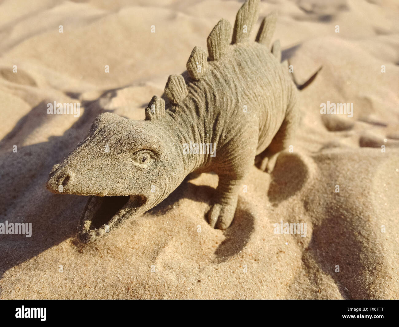 Spielzeug in Form von einem Dinosaurier stehend auf Sand. Stockfoto