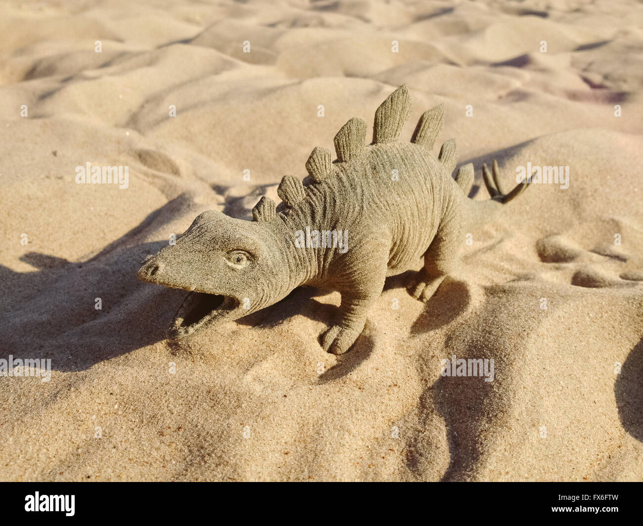 Spielzeug in Form von einem Dinosaurier stehend auf Sand. Stockfoto