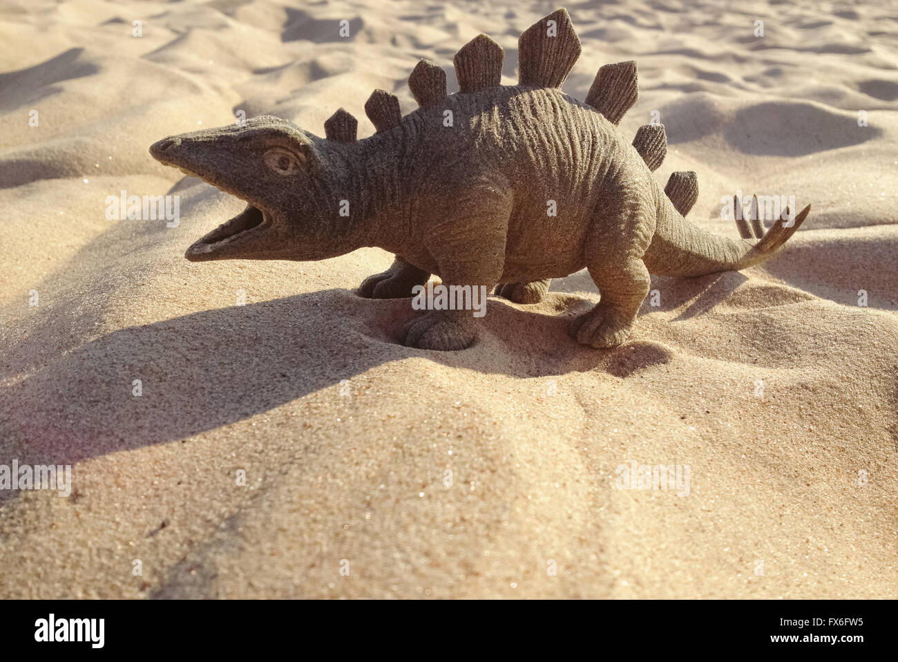 Spielzeug in Form von einem Dinosaurier stehend auf Sand. Stockfoto