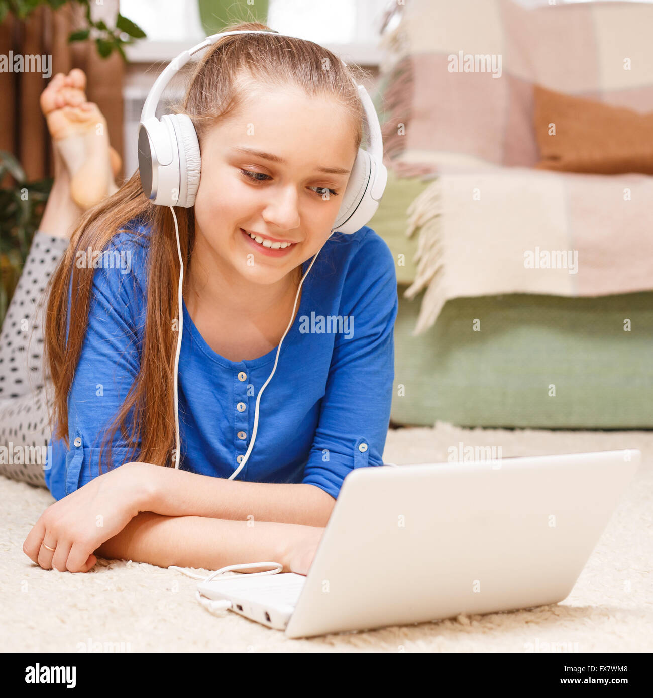 Lächelnden Mädchens mit weißen Kopfhörer mit Laptop auf dem Boden. Lächelnde Teenager studieren mit Laptop zu Hause. Online-edu Stockfoto
