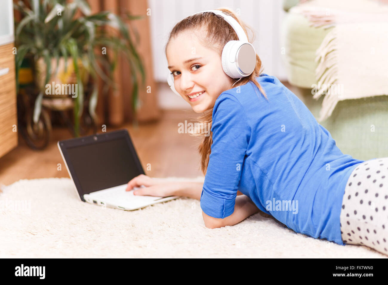 Lächelnden Mädchens mit weißen Kopfhörer mit Laptop auf dem Boden. Teenager auf der Suche in die Kamera Lächeln. Online-Bildung bac Stockfoto