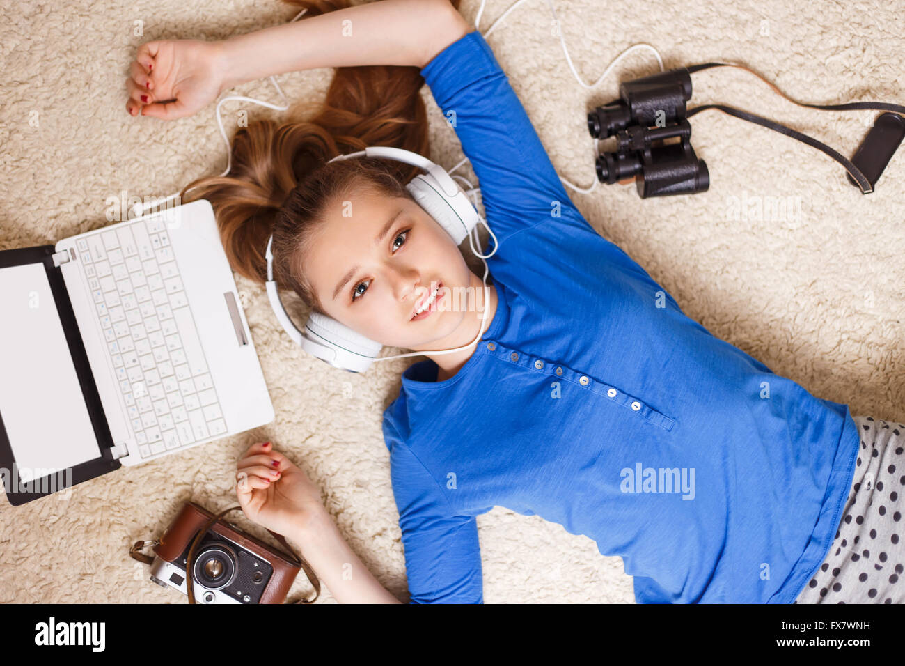Junge lächelnde Teenager-Mädchen in Kopfhörer Ohrhörer mit Laptop Kamera und Fernglas auf dem Boden liegend. Glücklich träumen teenager Stockfoto