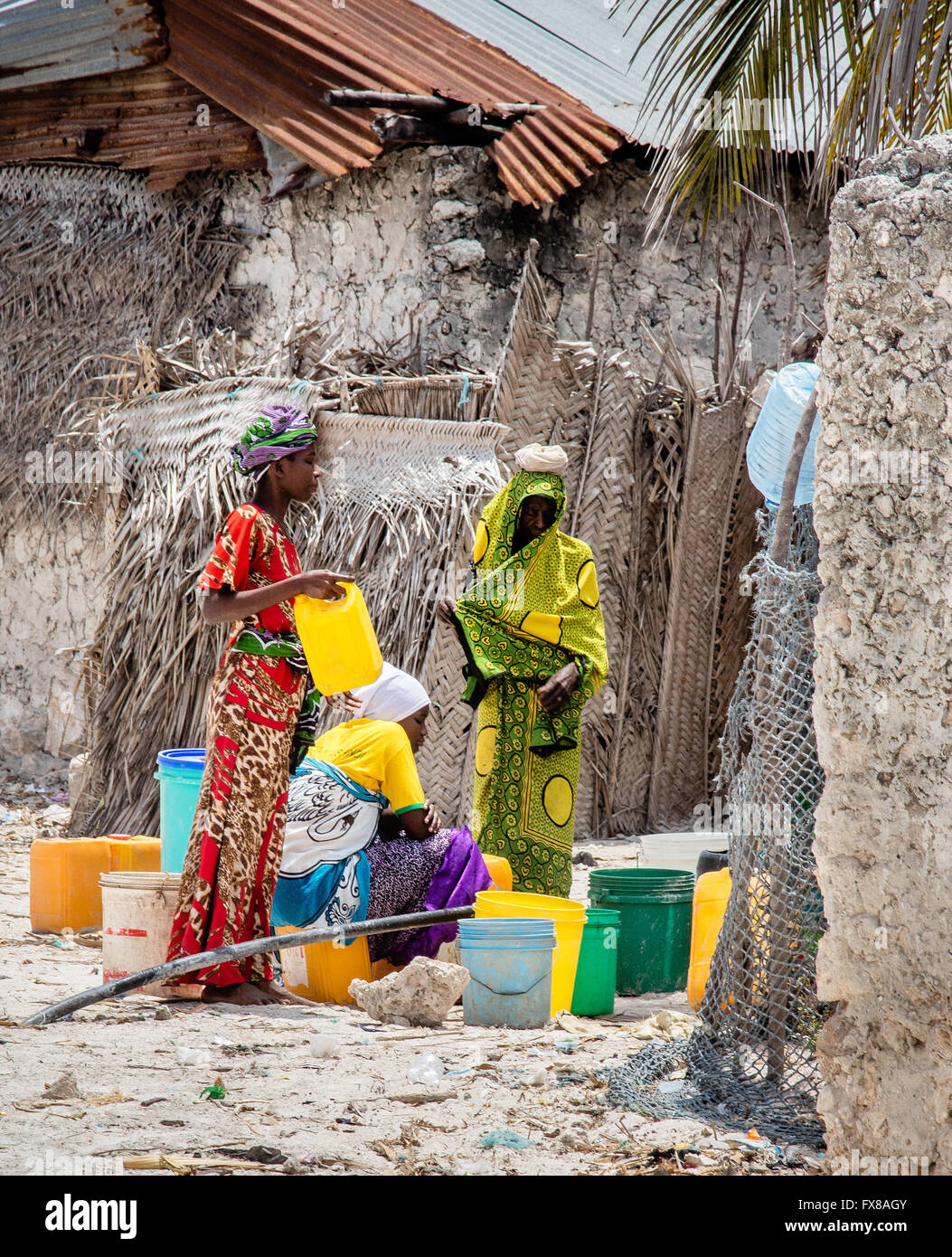 Bunt gekleidet Frauen sammeln Wasser in Kunststoff-Behältern aus einem kommunalen Hahn in einem tansanischen Dorf auf Zanzibar-Ostafrika Stockfoto