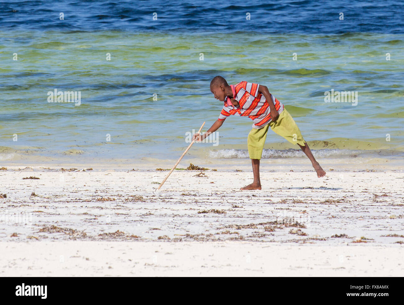 Ein kleiner Junge mit einem Stock zeichnet eine Linie im Sand des Strandes an der Ostküste von Zanzibar-Ostafrika Stockfoto