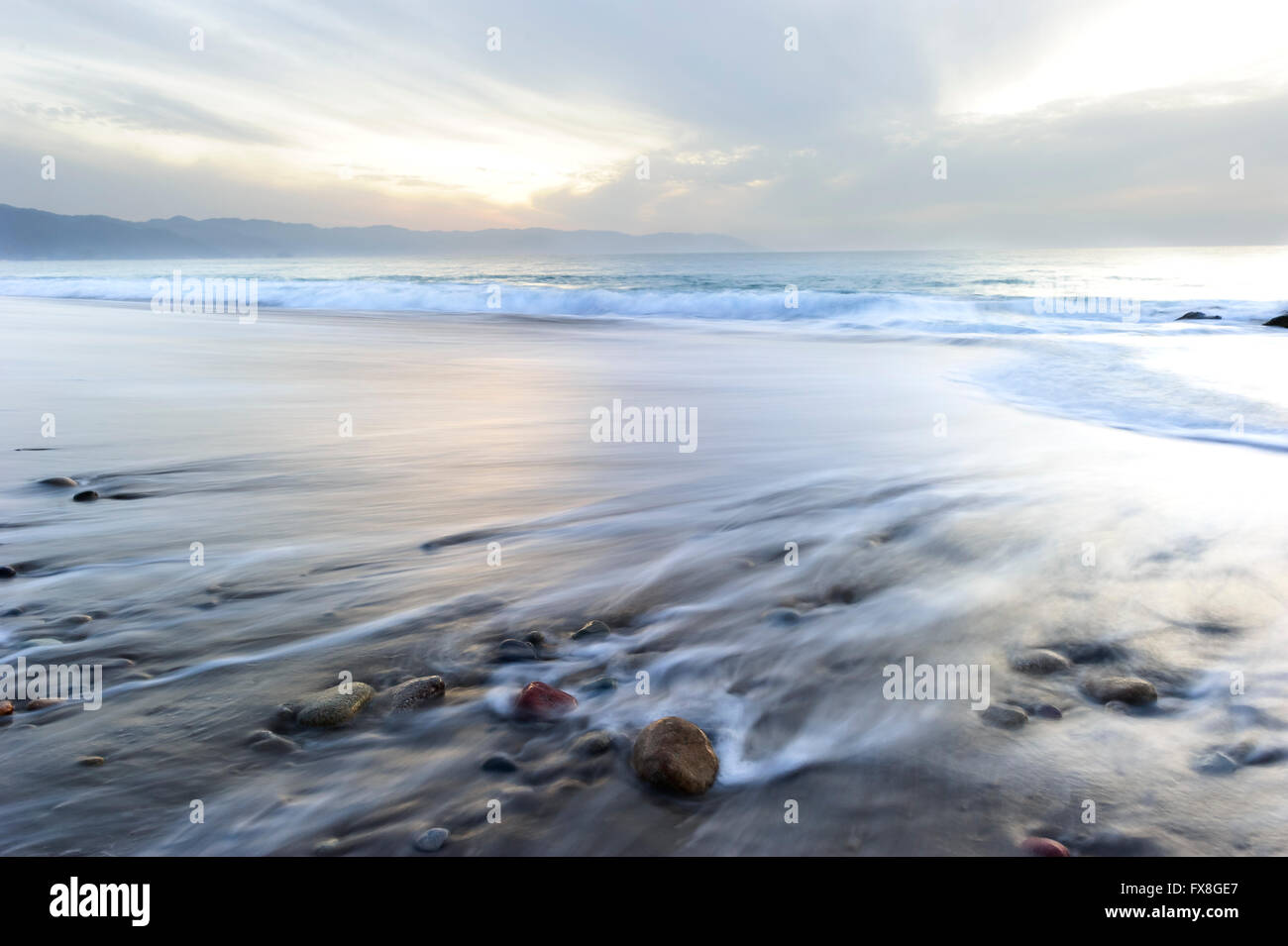 Meer Sonnenuntergang Strand Wellen ist ein Bilder von einem Ansturm von Wellen, die durch eine Langzeitbelichtung mit einer leuchtenden roten Sonnenuntergang Wolke gefüllt Himmel erfasst Stockfoto