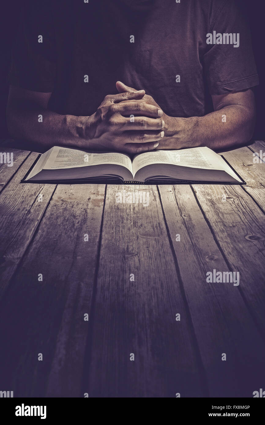 Mann, der betet auf einem Holztisch mit einer geöffneten Bibel. Stockfoto