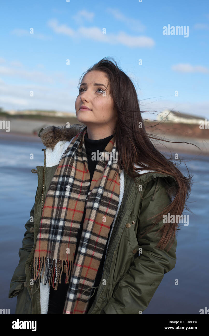 Schöne junge Frau, die auf der Suche nach oben an einem kalten, windigen Tag am Strand zu stehen Stockfoto