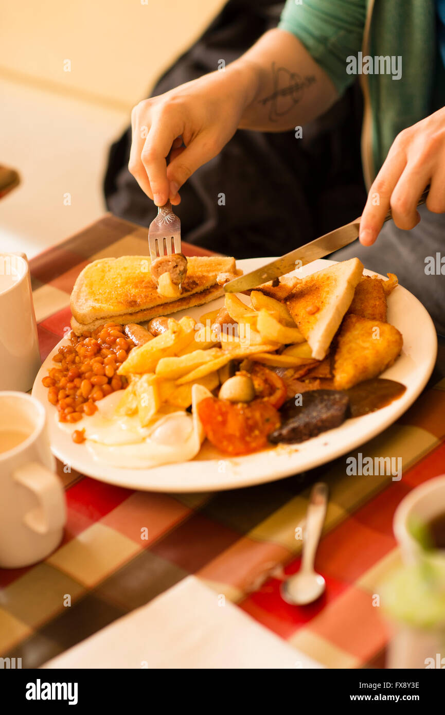 Ein junger Mann, ein komplettes englisches Frühstück - Eiern, Würstchen, Bohnen, Blutwurst, Chips, Tomaten, Toast, - in der Express Cafe Essen, besaß ein kleinen selbstständig Fisch und Pommesbude. Aberystwyth Wales UK Stockfoto