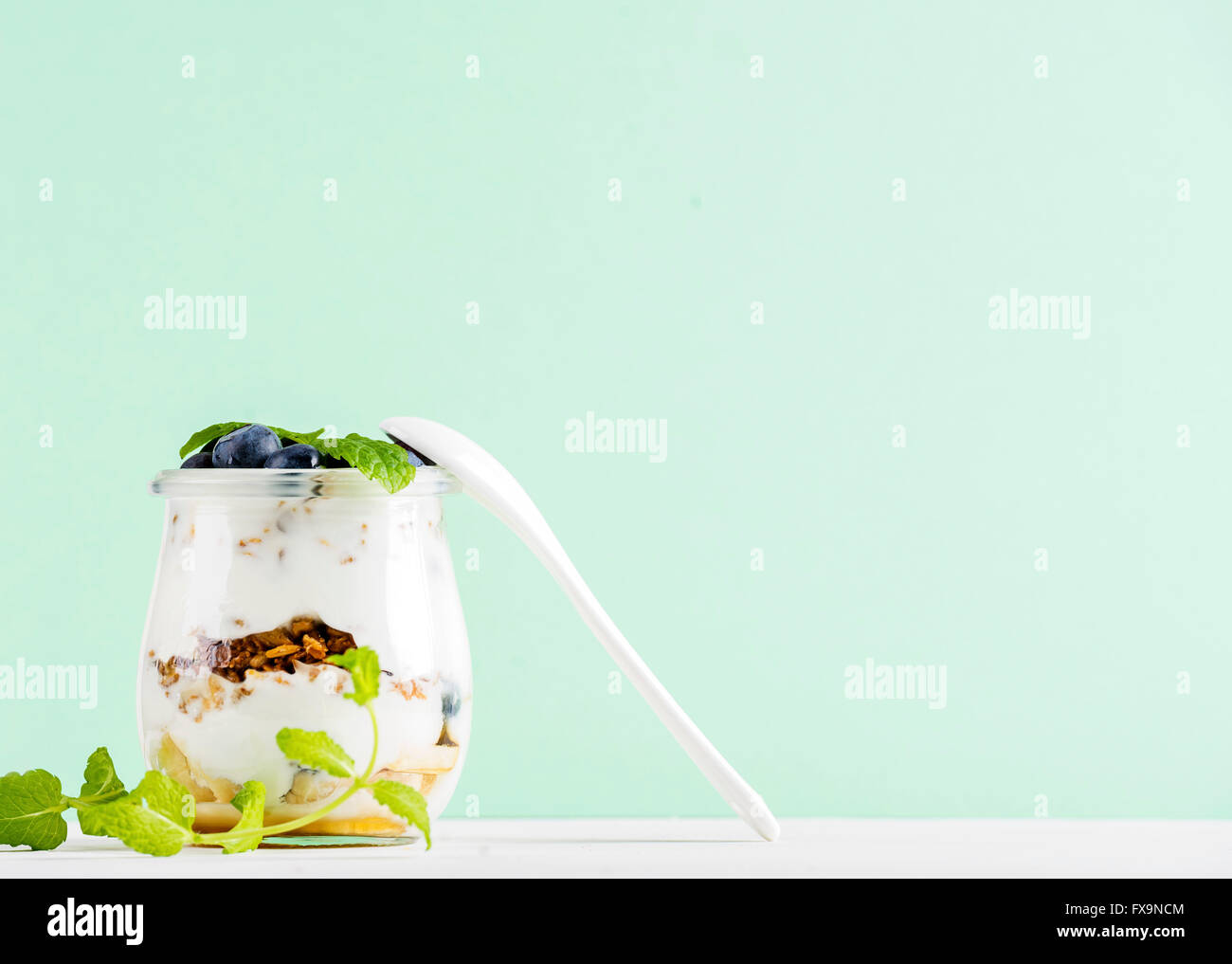 Joghurt und Hafer-Müsli mit Marmelade und Heidelbeeren im Glas auf Pastell Mint Hintergrund, Tiefenschärfe, Textfreiraum Stockfoto