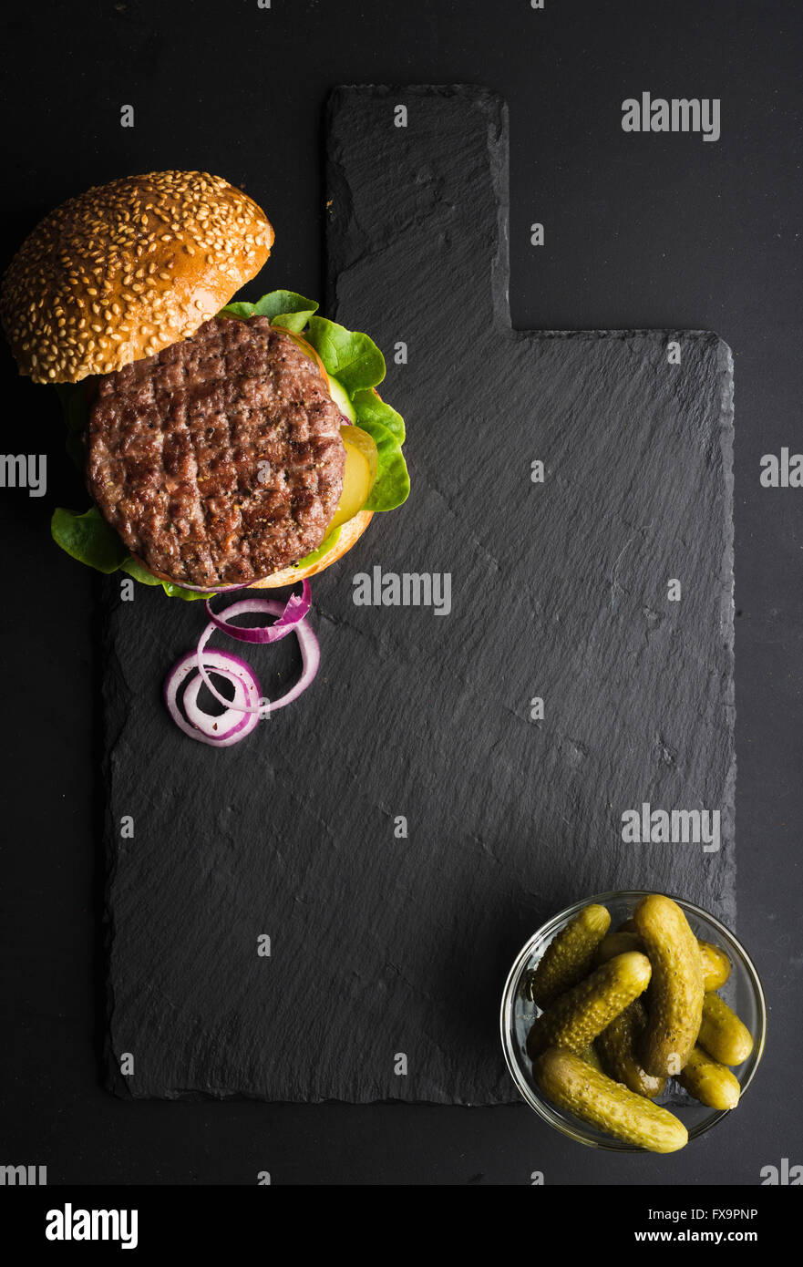 Frische hausgemachte Burger auf dunklen Schiefer Steinplatte, Pickles und in Scheiben geschnittene Zwiebel auf schwarzem Hintergrund. Ansicht von oben, Textfreiraum Stockfoto