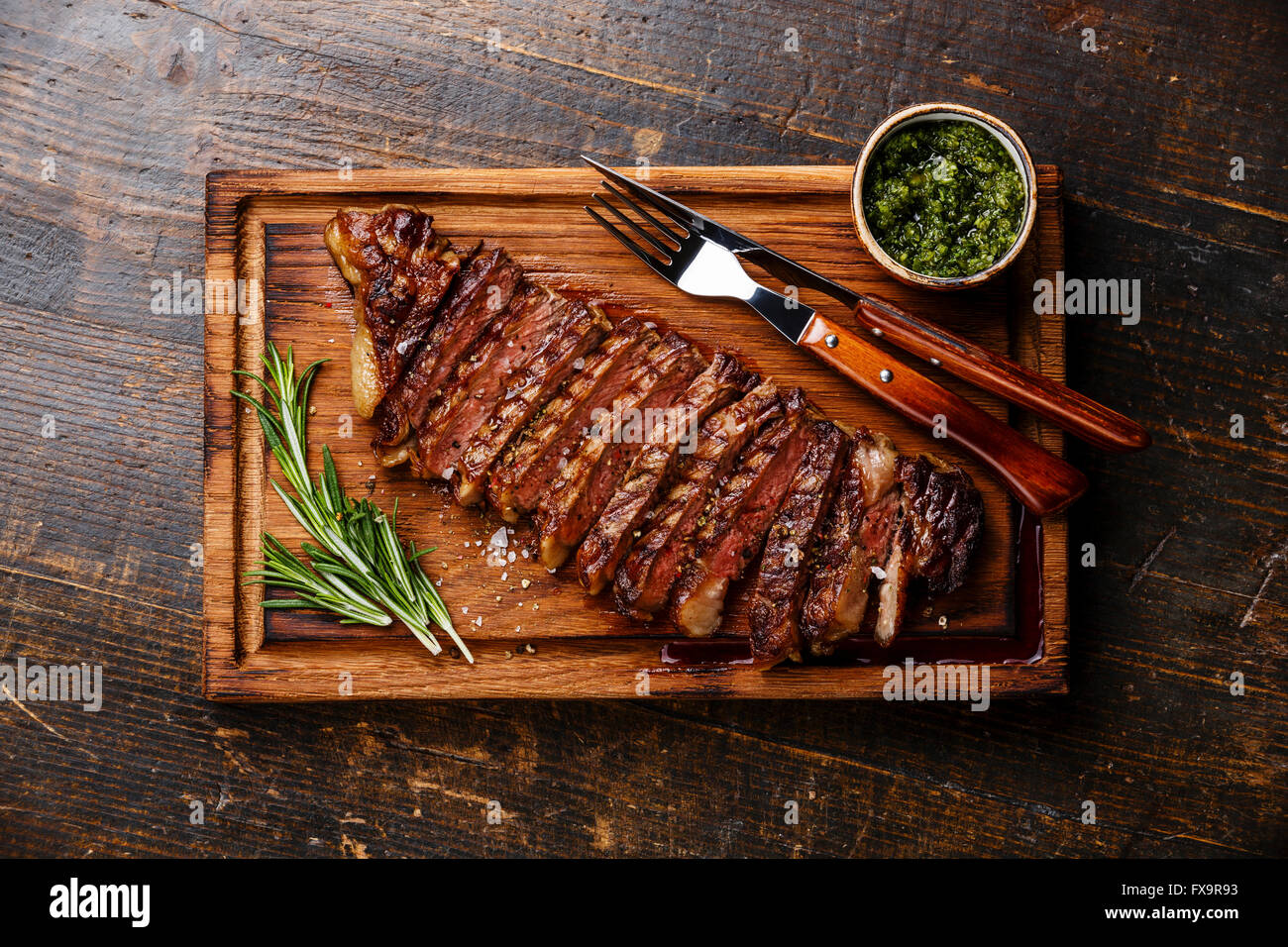 Gegrilltes Rindfleisch Grill Striploin Steak mit Chimichurri-Sauce auf Schneidebrett auf dunklem Holz geschnitten Stockfoto
