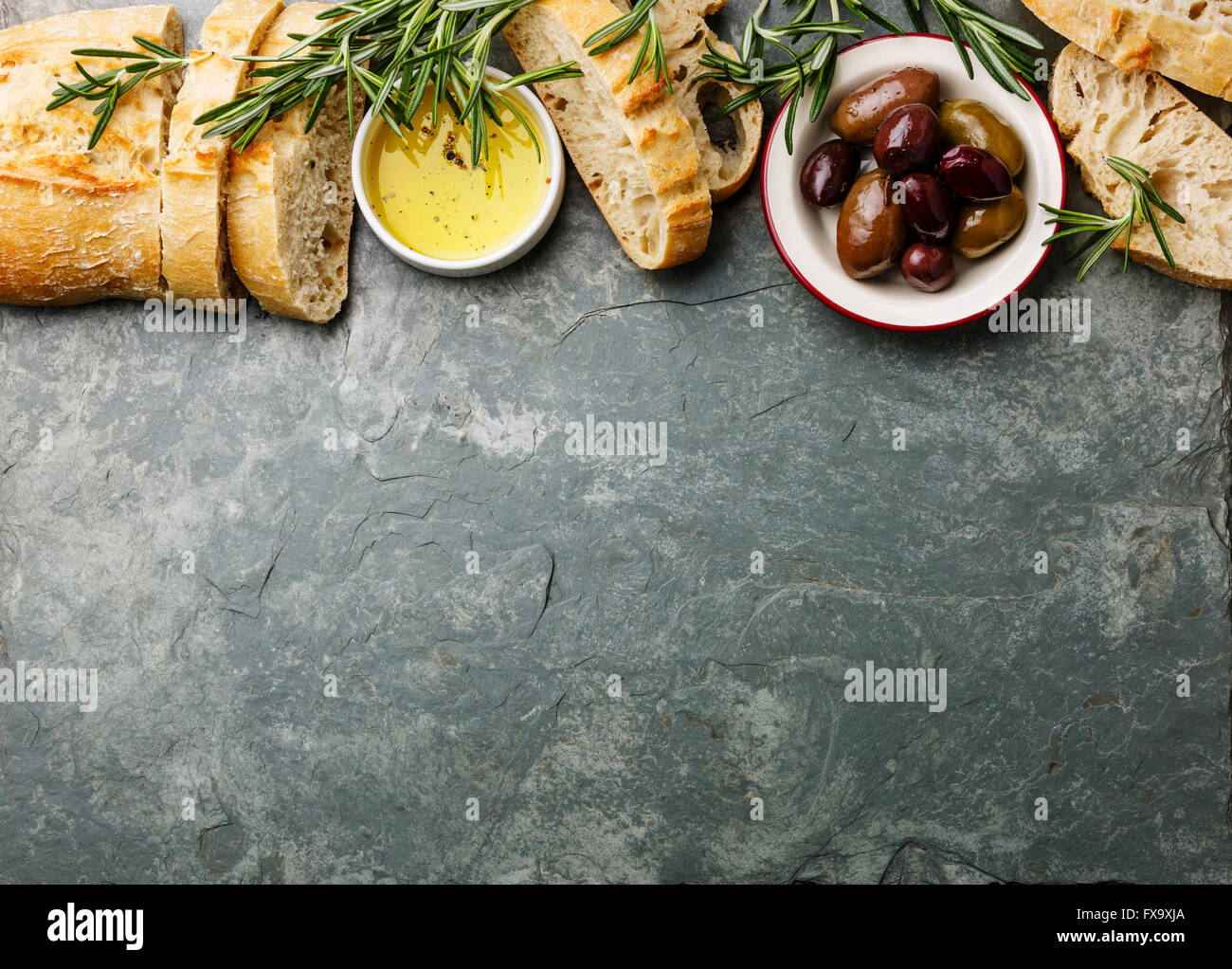 Italienische Küche Zutaten Hintergrund mit Geschnetzeltes Brot Ciabatta, Olivenöl, Oliven und Rosmarin auf grauem Stein Schiefer Stockfoto