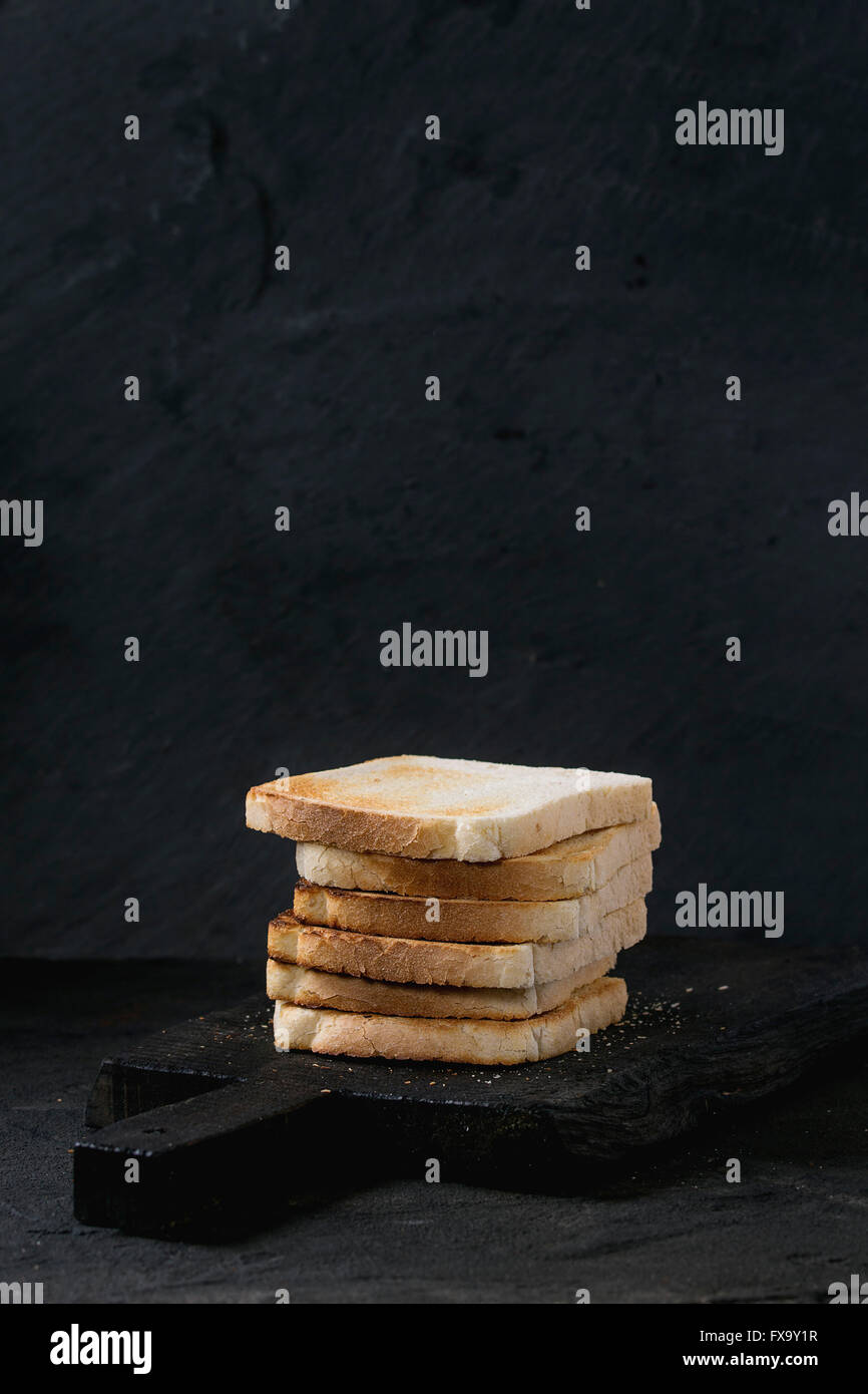 Haufen von frischem Toast Brot auf schwarzen Holzbrett über schwarz strukturierten Hintergrund. Stockfoto
