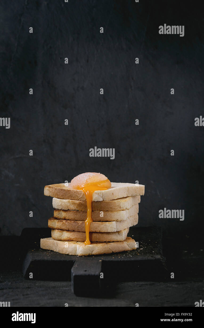 Haufen von Toast-Brot mit fließenden gezuckert Eigelb auf schwarzen Holzbrett über schwarz strukturierten Hintergrund. Stockfoto