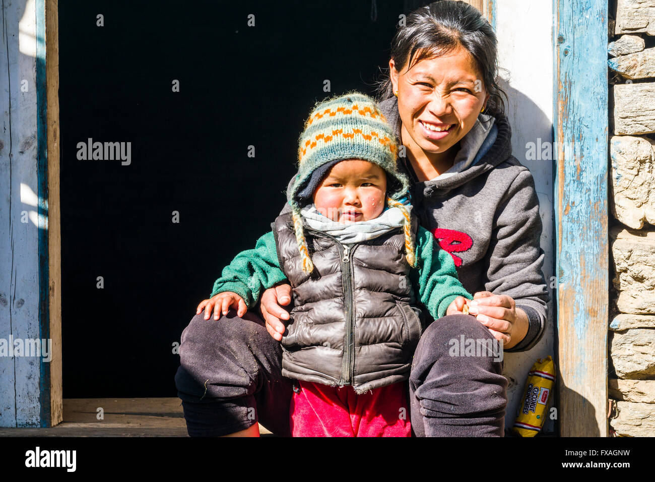 Porträt einer lächelnden jungen Nepali Mutter mit ihrem Kind sitzen in einem Hauseingang, Chheplung, Solo Khumbu, Nepal Stockfoto