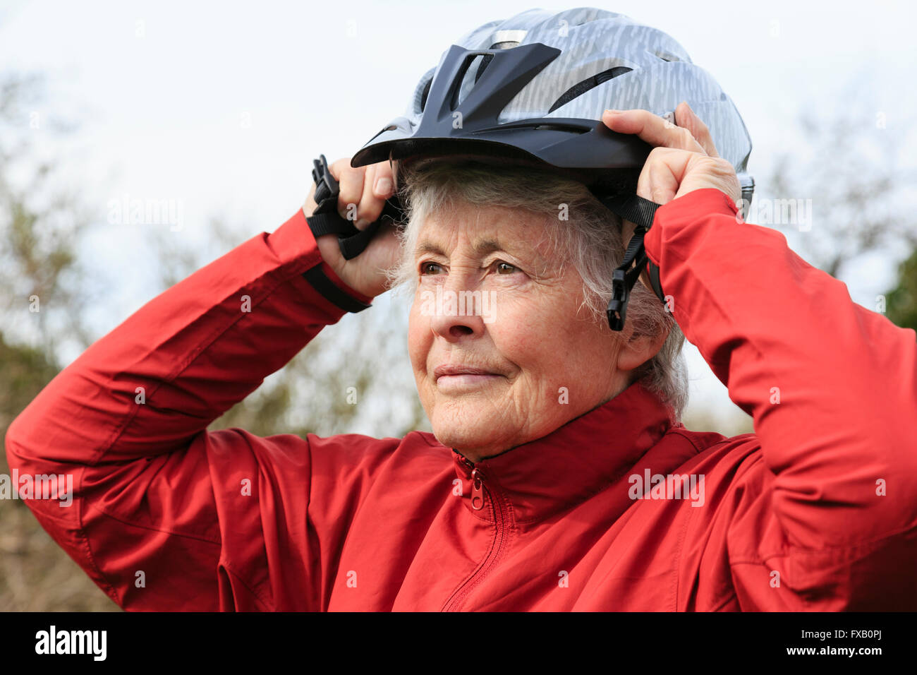 Aktive ältere ältere zog sich Frau setzen auf ein Fahrrad Helm die Vorbereitung für eine Fahrradtour, gesund in den Ruhestand zu gehen. England Großbritannien Stockfoto