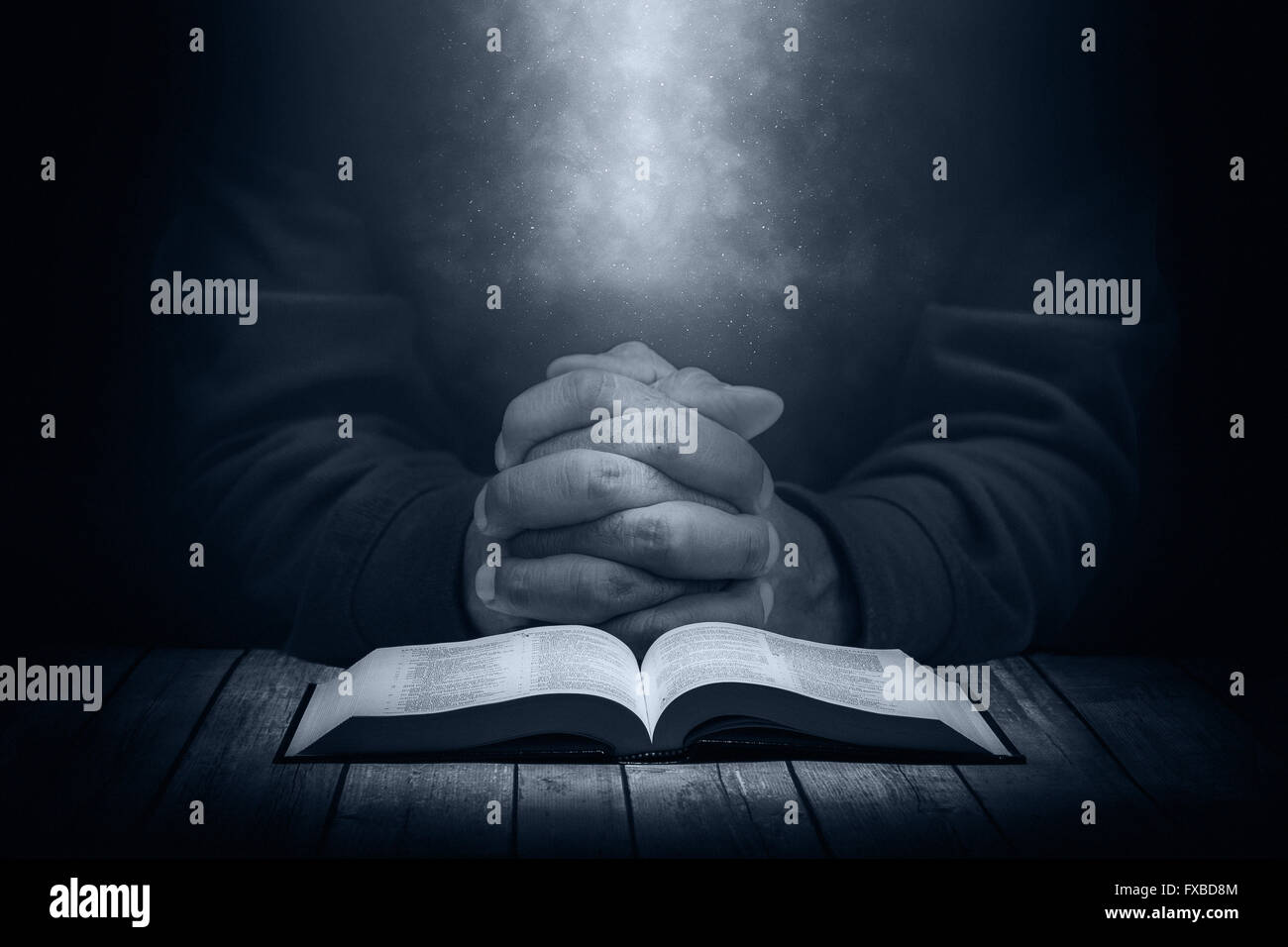 Mann, der betet auf einem Holztisch mit eine aufgeschlagene Bibel im Dunkeln. (Christian Concept). Stockfoto