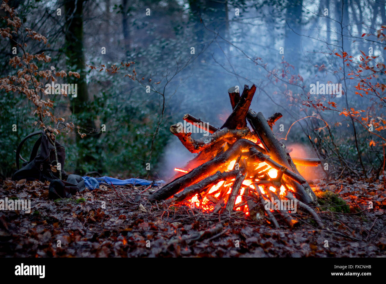 Eine glühende Lagerfeuer im Wald, mit Rucksack und Bäume im Hintergrund. Stockfoto