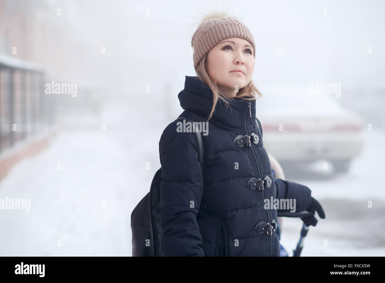 Junge Frau mit Kinderwagen zu Fuß im Winter schaut nachdenklich Himmel. Stockfoto