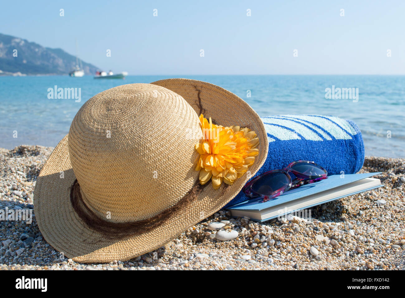 Strohhut-Sonnenbrillen, Handtuch und Buch am Strand Stockfoto