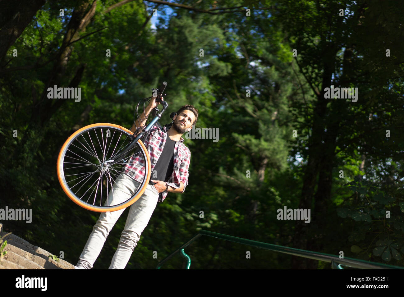 ein mächtiger Mann sein Motorrad auf der Schulter hängend auf Treppe, Blick weit entfernt bleiben. Stockfoto